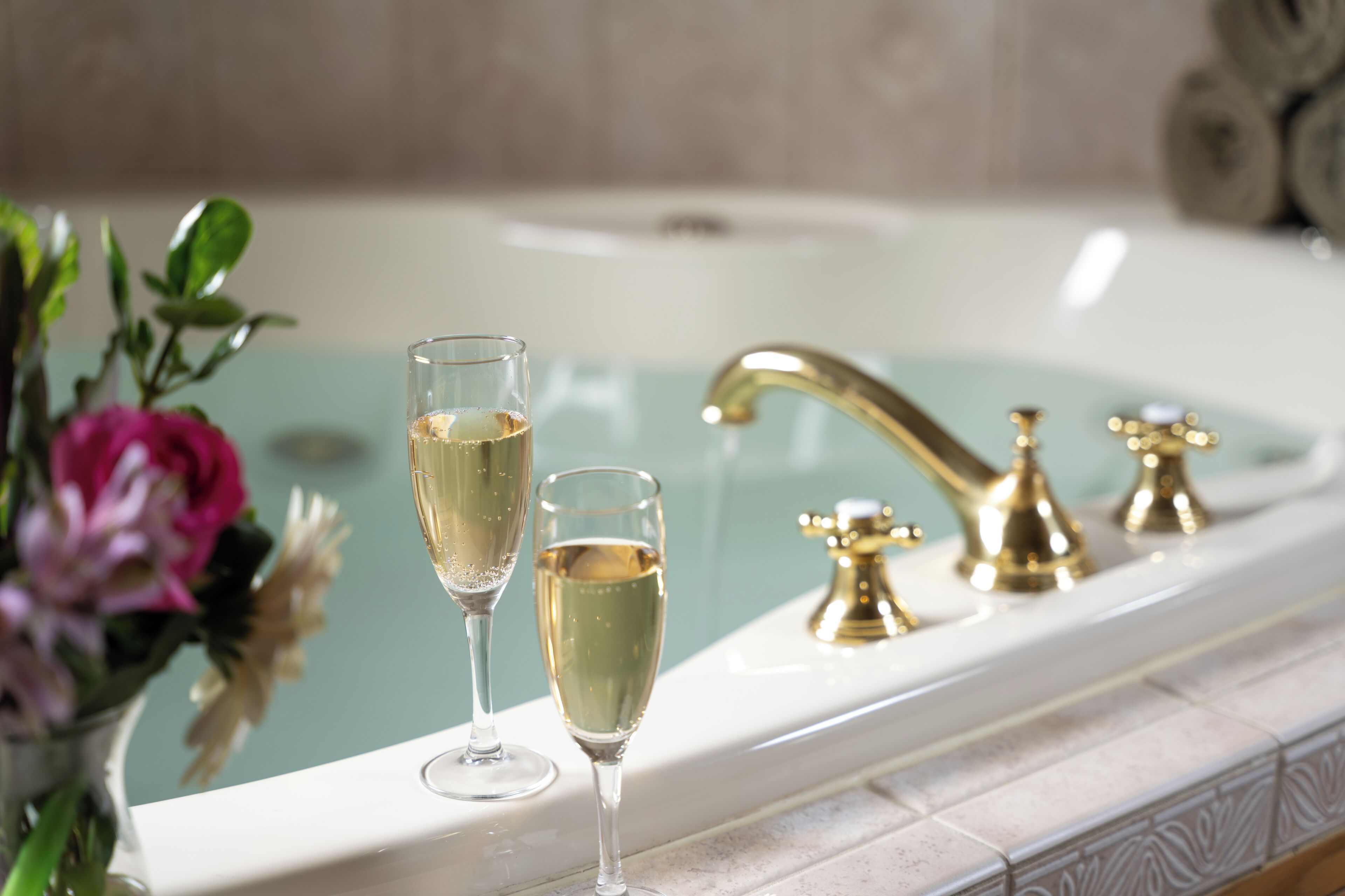 Une baignoire avec deux coupes à champagne et un robinet doré.