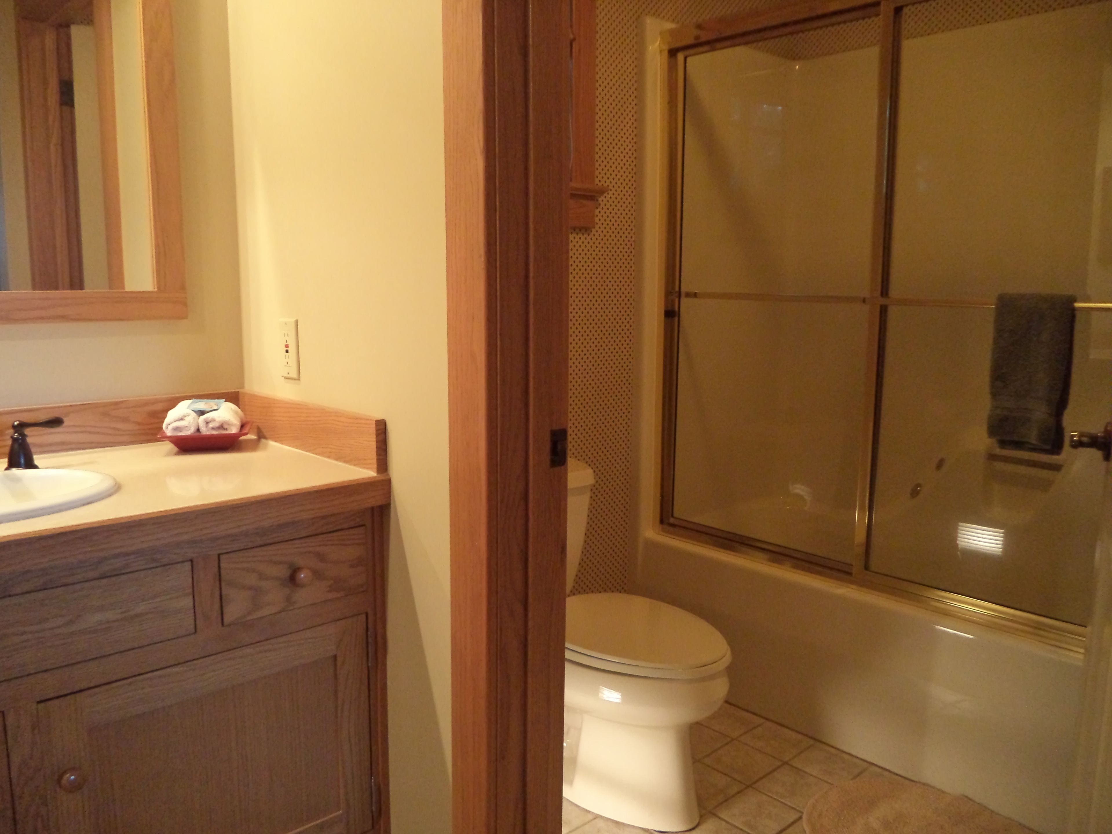 Un baño con tocador de madera, lavamanos blanco, inodoro y ducha con mampara de vidrio.
