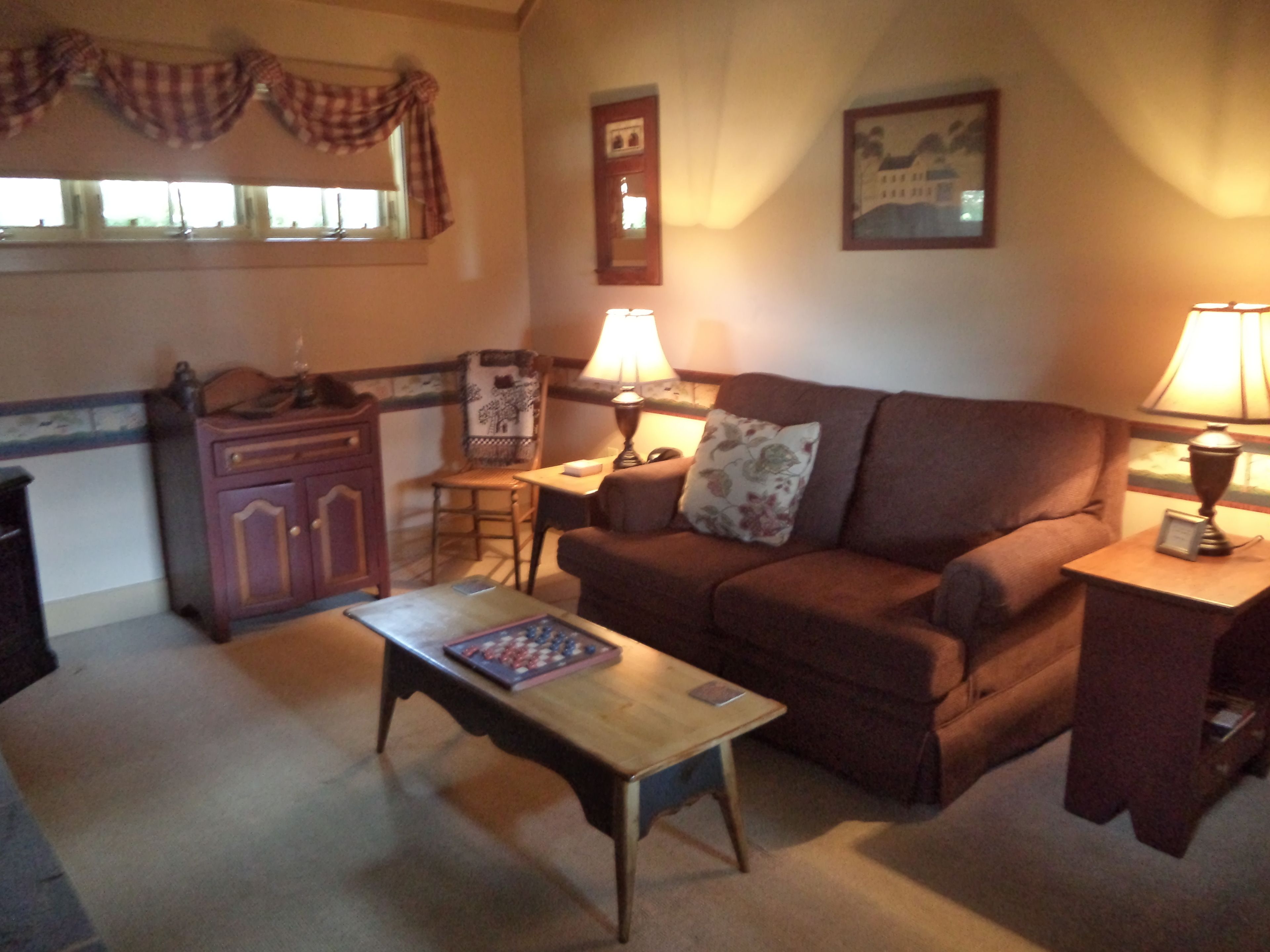 A cozy living room with a brown sofa, a wooden coffee table, a small table with a lamp, and a chair.