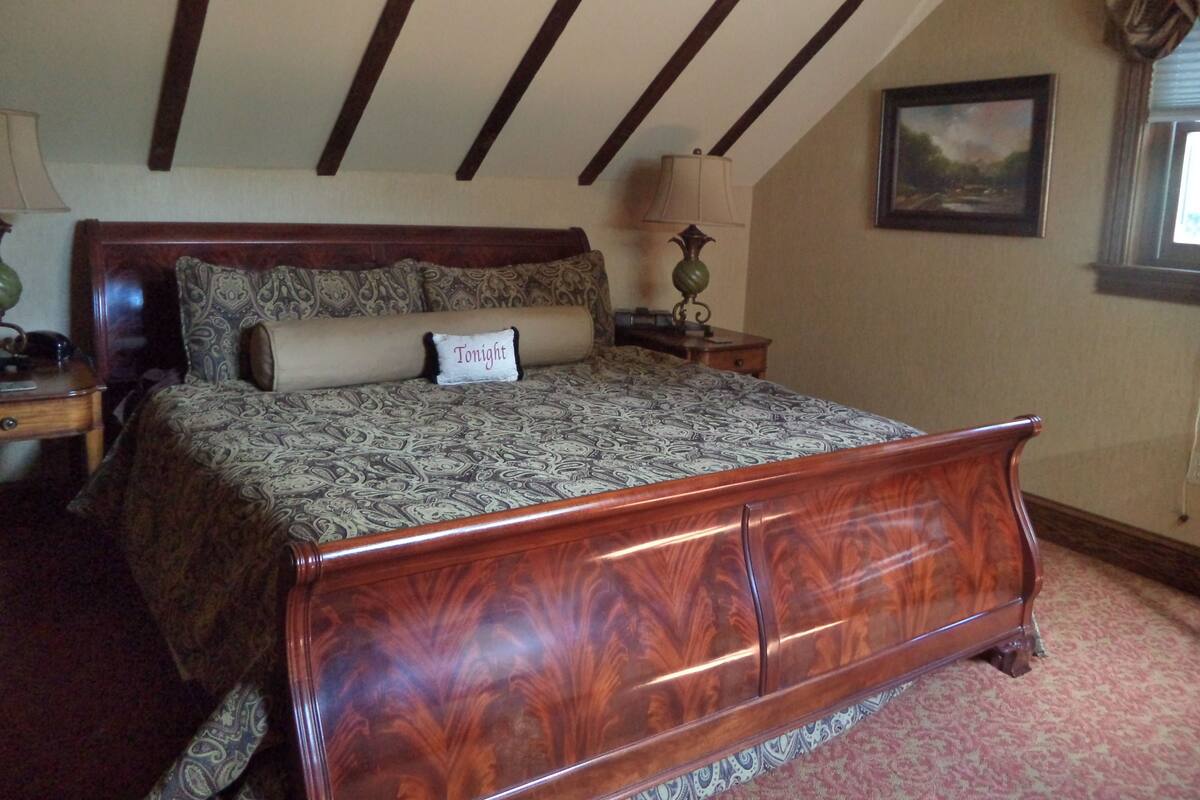 Una camera da letto con un ampio letto di legno, un comodino, una lampada e un quadro appeso al muro.