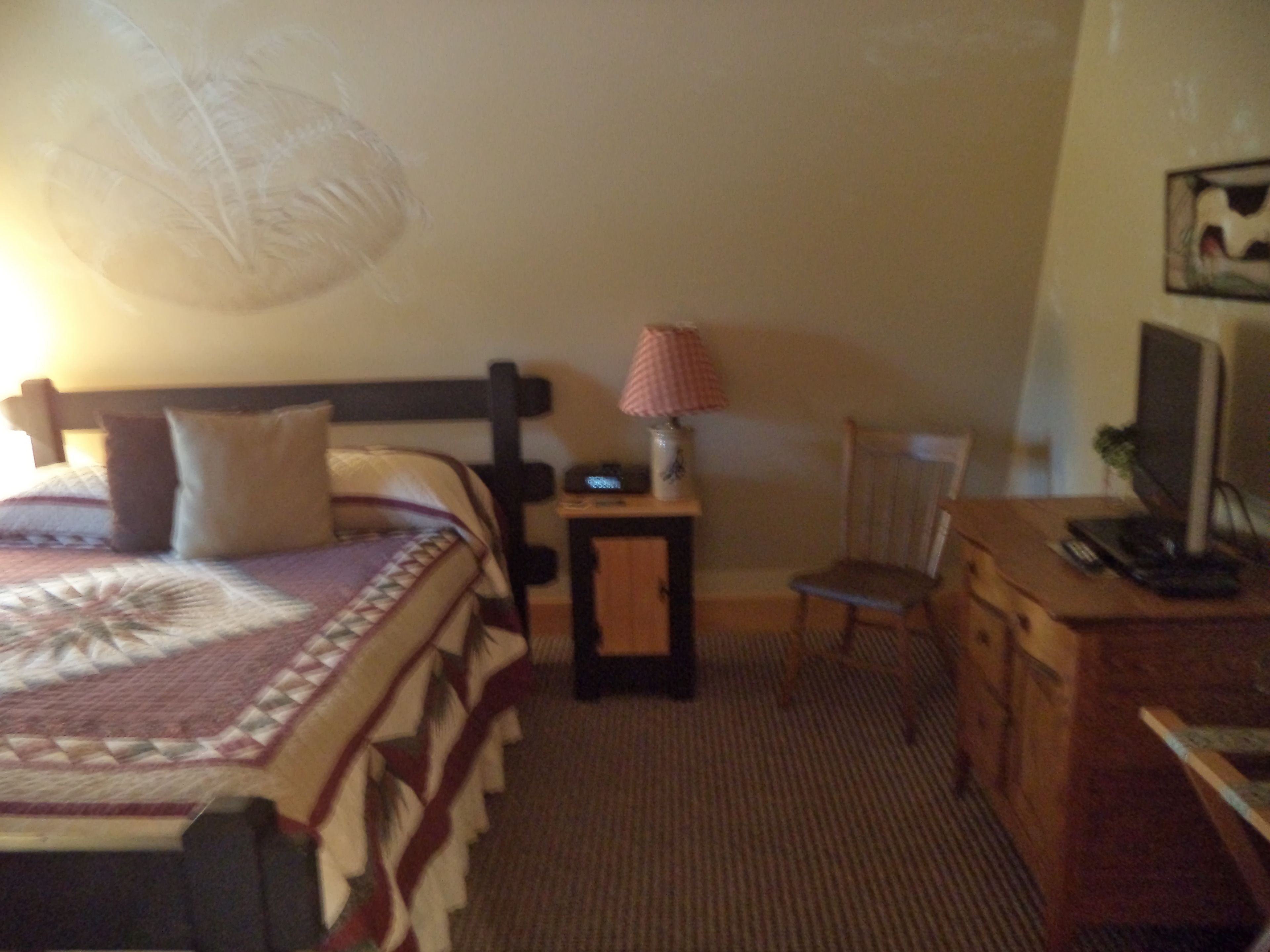 Quarto de hotel com cama, escrivaninha, cadeira e televisão.