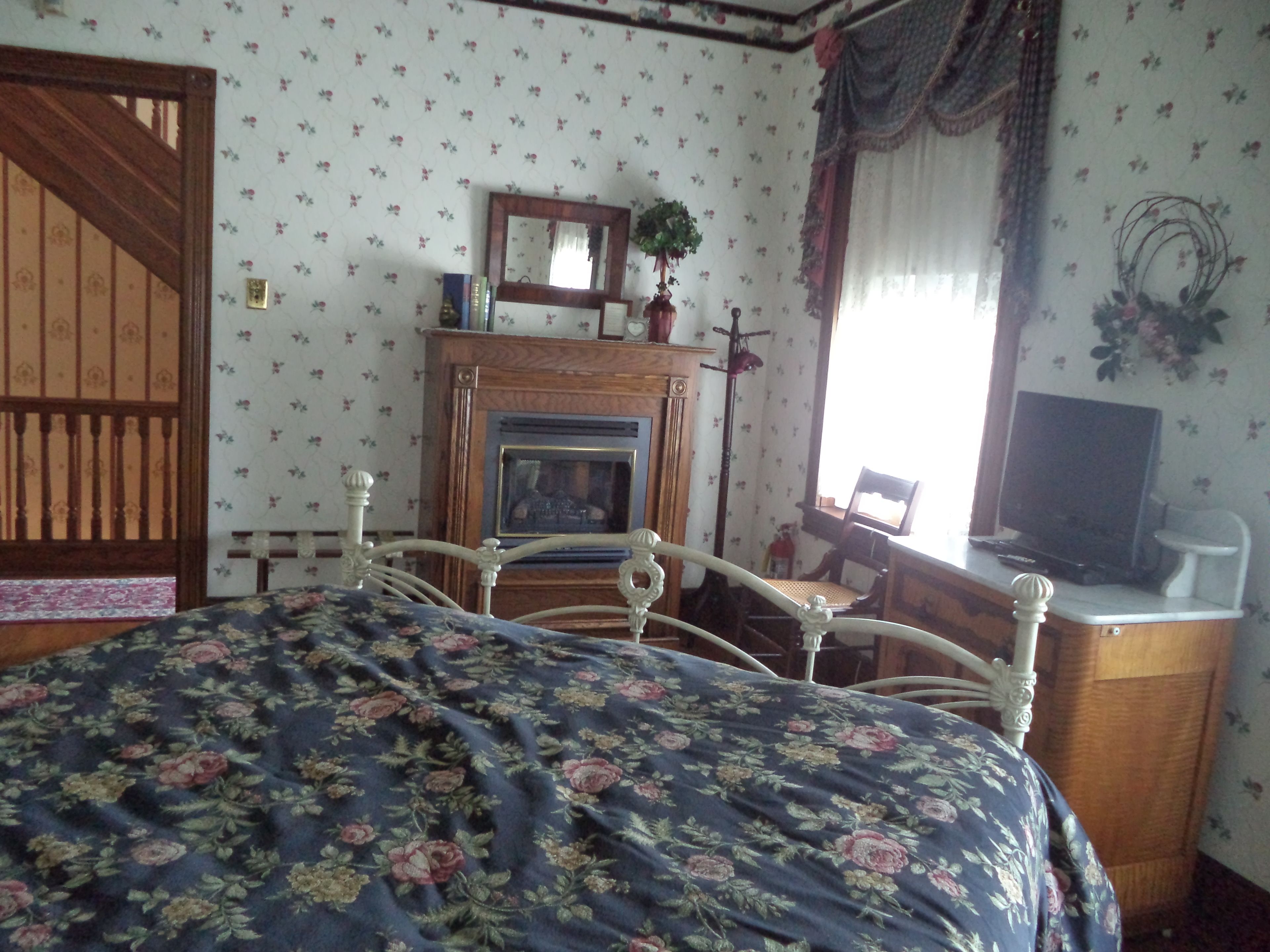 Un dormitorio con cama, cómoda de madera, televisión, chimenea y ventana con cortinas.