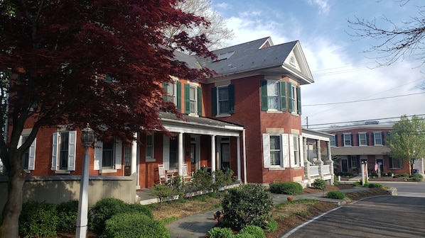 A two-story brick house with a porch, green shutters, and a well-maintained lawn.