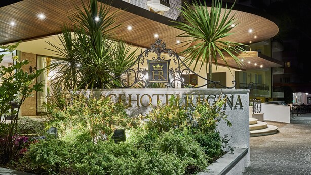 A hotel entrance with a sign reading "Hotel Regina," surrounded by lush greenery and a modern architectural design.