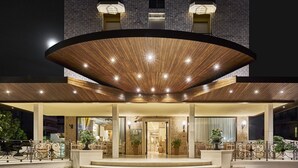 A hotel entrance with a curved wooden canopy, steps leading up to the entrance, and outdoor seating with potted plants.