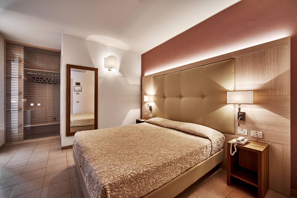 Une chambre d’hôtel avec un grand lit, une tête de lit en bois, des lampes de chevet, un téléphone et une armoire avec un miroir.