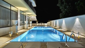 A rectangular outdoor swimming pool with clear blue water, surrounded by lounge chairs and potted plants.