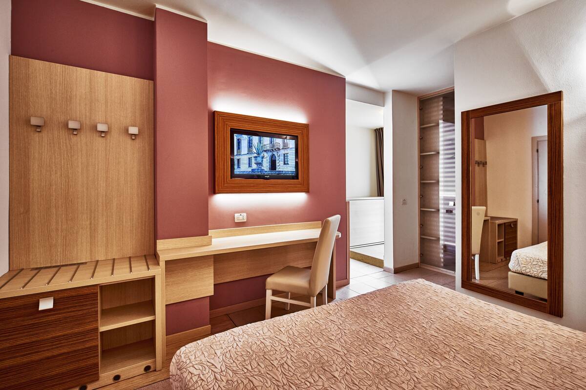 Une chambre à coucher comprenant un lit, un bureau, une chaise, une armoire et un miroir.