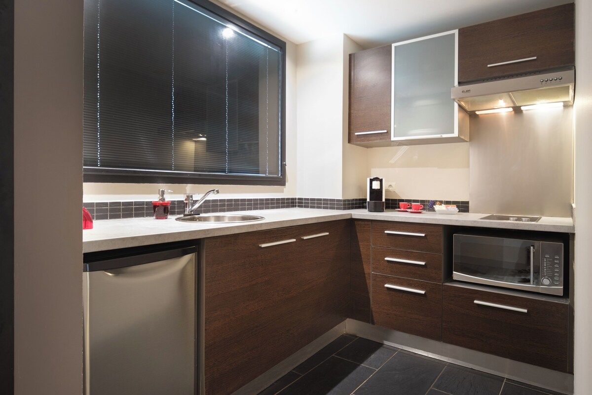 A compact kitchen with a built-in dishwasher, a microwave, and a window with blinds.