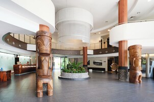 Un hall d’entrée spacieux, doté de piliers en bois, d’un comptoir d’accueil et d’un grand bac à plantes au centre, agrémenté de verdure.