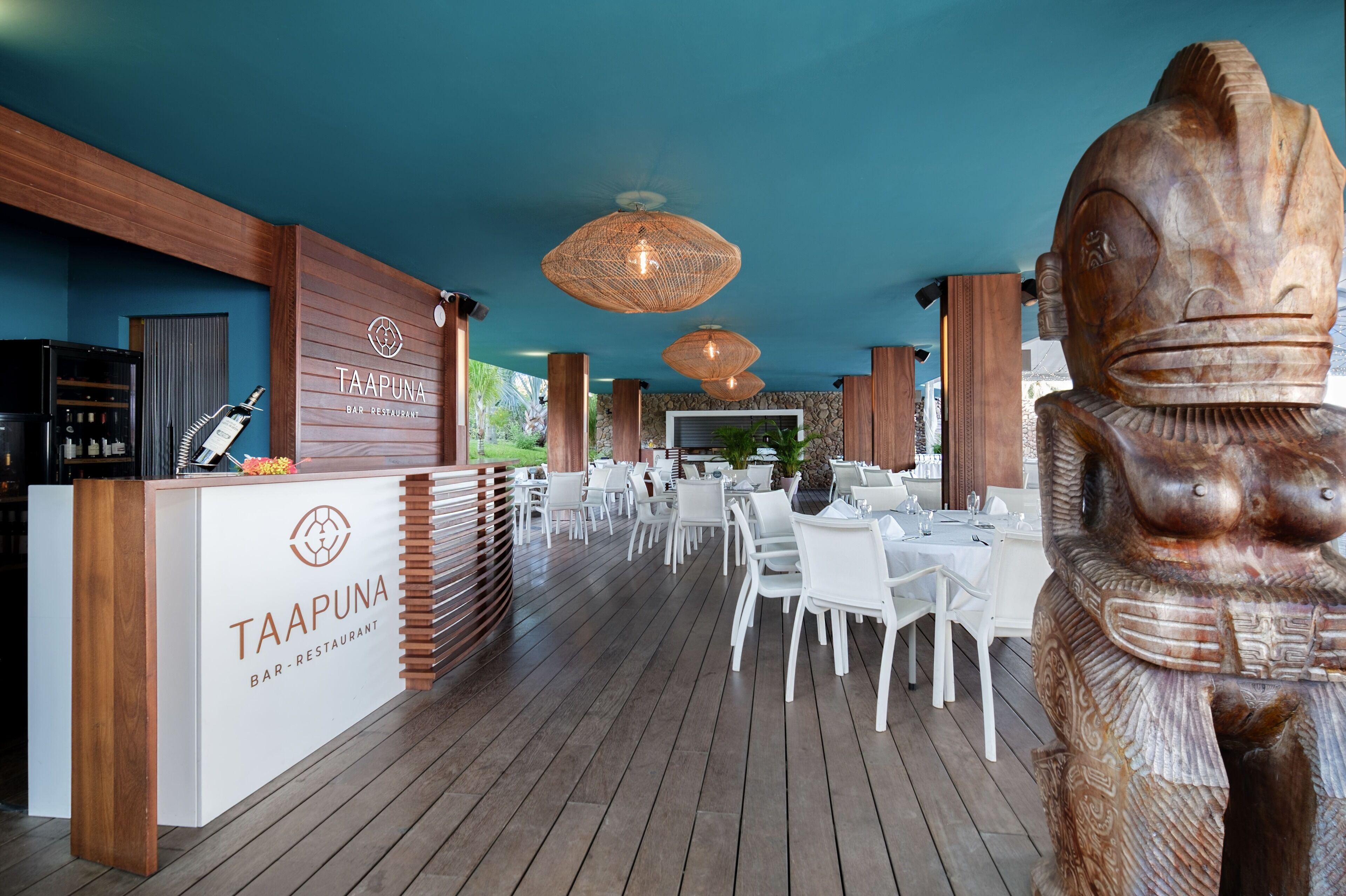 Un restaurante con mostrador de recepción de madera, sillas blancas y una gran escultura de madera.