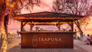 A beach bar named Taapuna Beach Bar with a wooden structure and string lights.