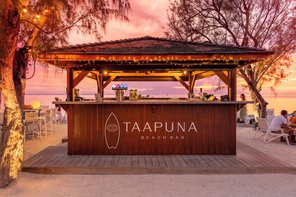 Un bar de playa llamado Taapuna Beach Bar, con estructura de madera y luces colgantes.