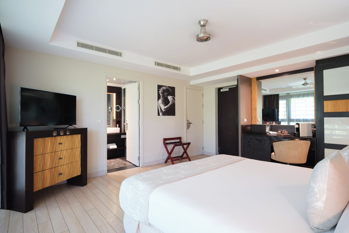 Una moderna camera d'hotel con un letto grande, una televisione, un armadio in legno e un piccolo angolo relax.