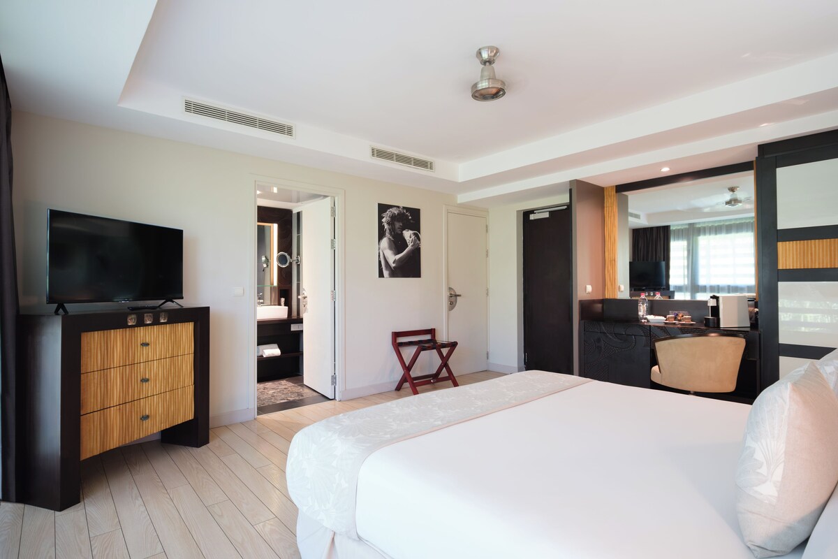 A modern hotel room with a large bed, a TV, a wooden cabinet, and a small seating area.