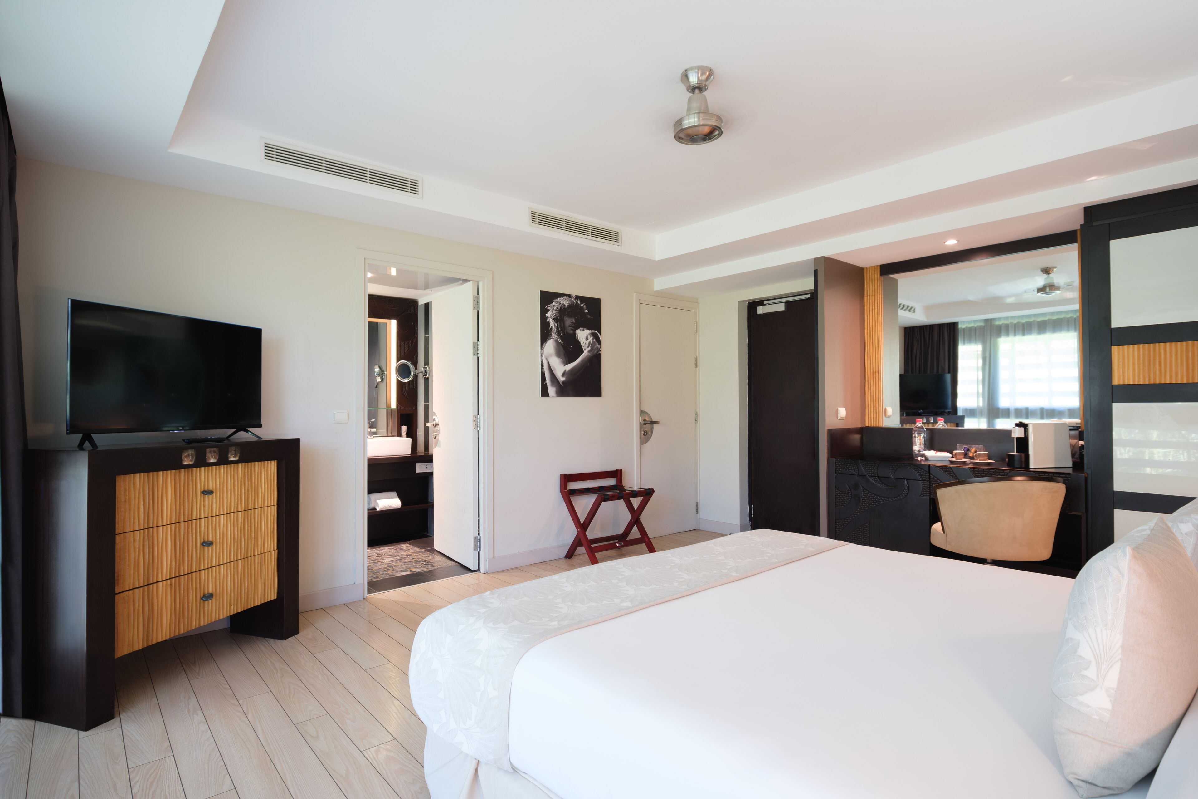 A modern hotel room with a large bed, a TV, a wooden cabinet, and a small seating area.