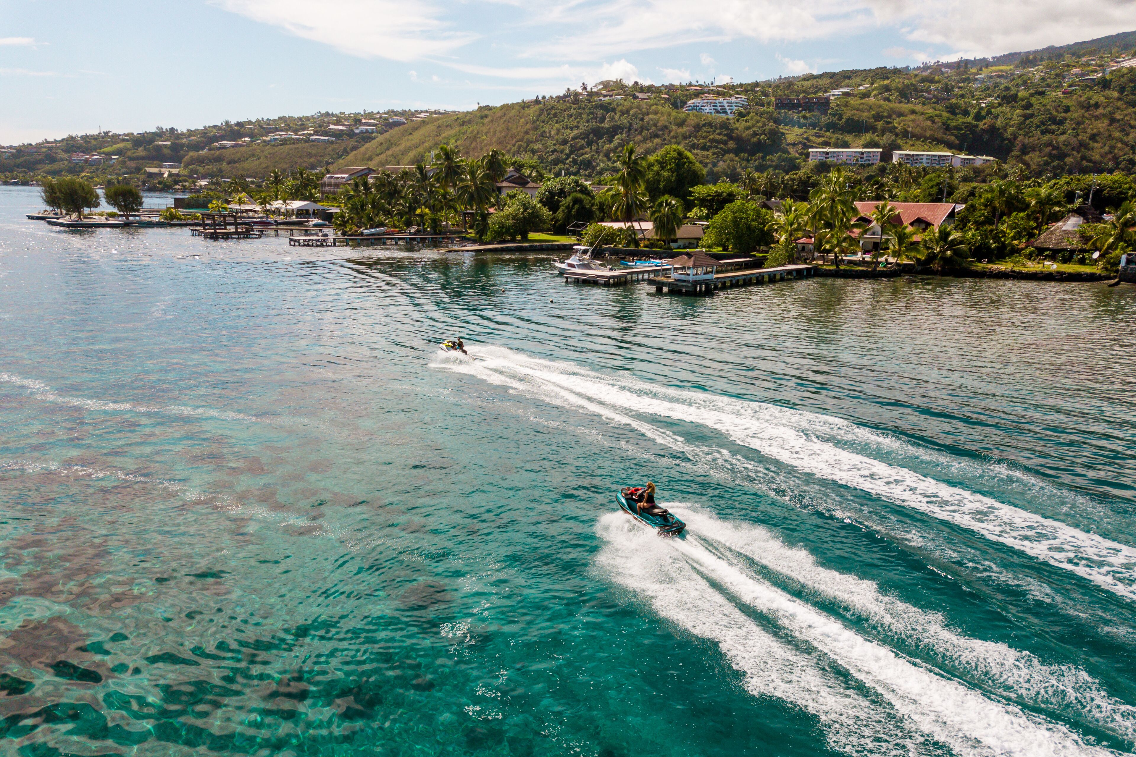 Una zona costiera con acque turchesi cristalline, un jet ski e un pontile con barche.