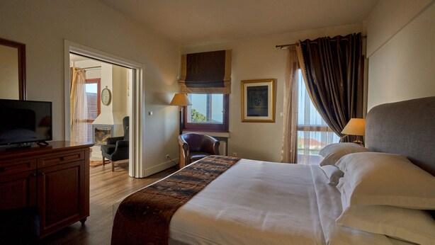 A hotel room with a bed, a television, a desk, a chair, and a window with curtains. - Xenia Palace Portaria (Volos)