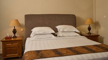 A neatly made bed with white linens, two bedside tables with lamps, and a wooden nightstand with a telephone.