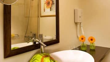 Un baño con un lavamanos blanco, un espejo, un perchero para toallas y un florero.