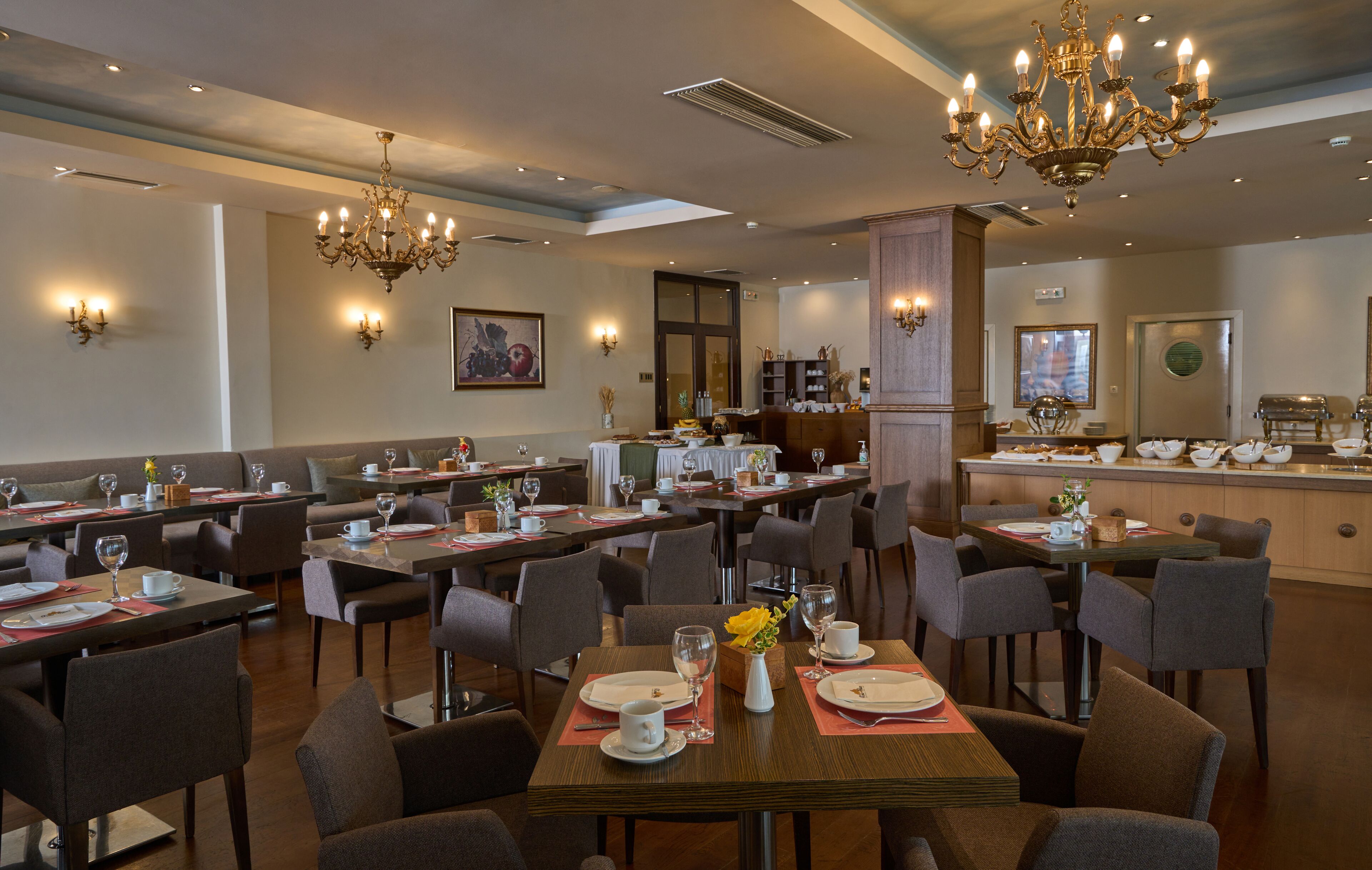 A spacious restaurant with multiple dining tables and chairs, elegant chandeliers, and wall sconces.