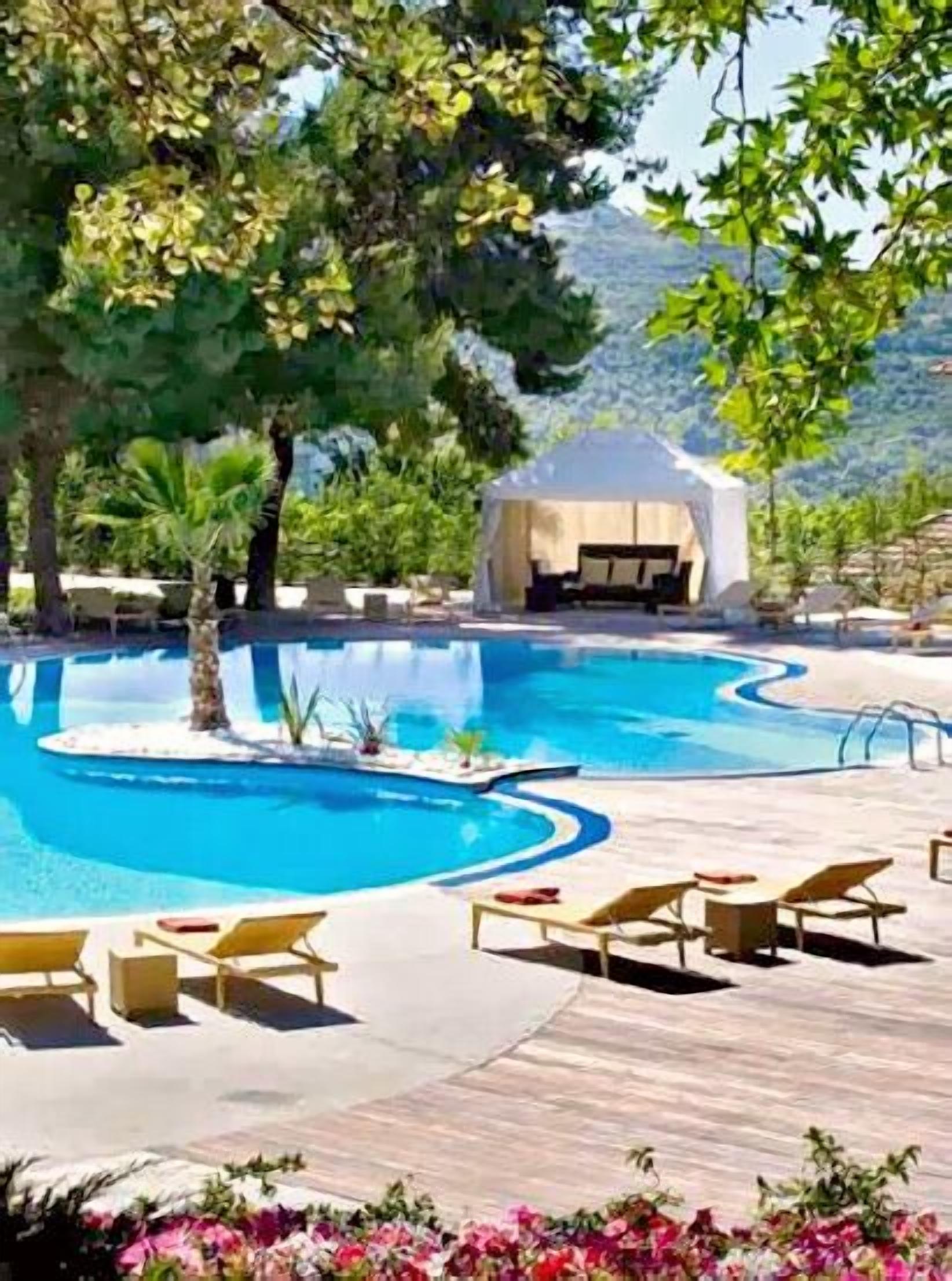 A pool area with lounge chairs, a covered seating area, and a mountainous backdrop.