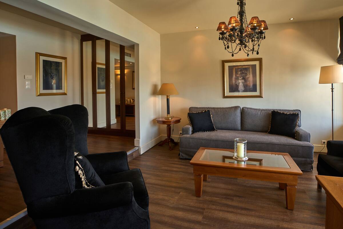 A living room with a sofa, two armchairs, a coffee table, a chandelier, and a painting on the wall.