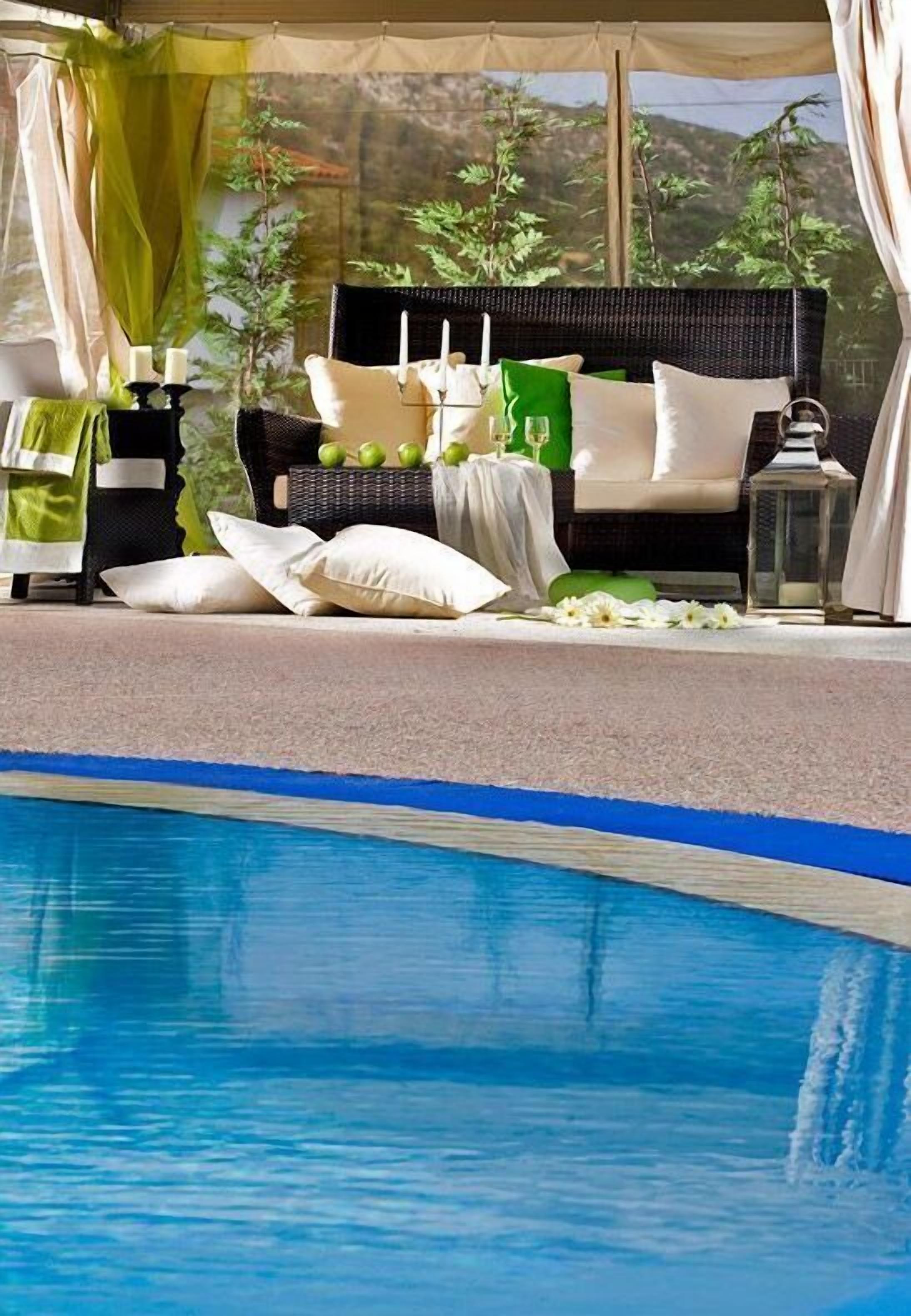 A poolside seating area with a wicker sofa, cushions, and a small table with candles.