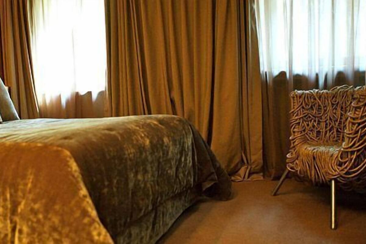A large bed with a textured blanket, a chair with a woven design, and curtains in a room with a warm ambiance.
