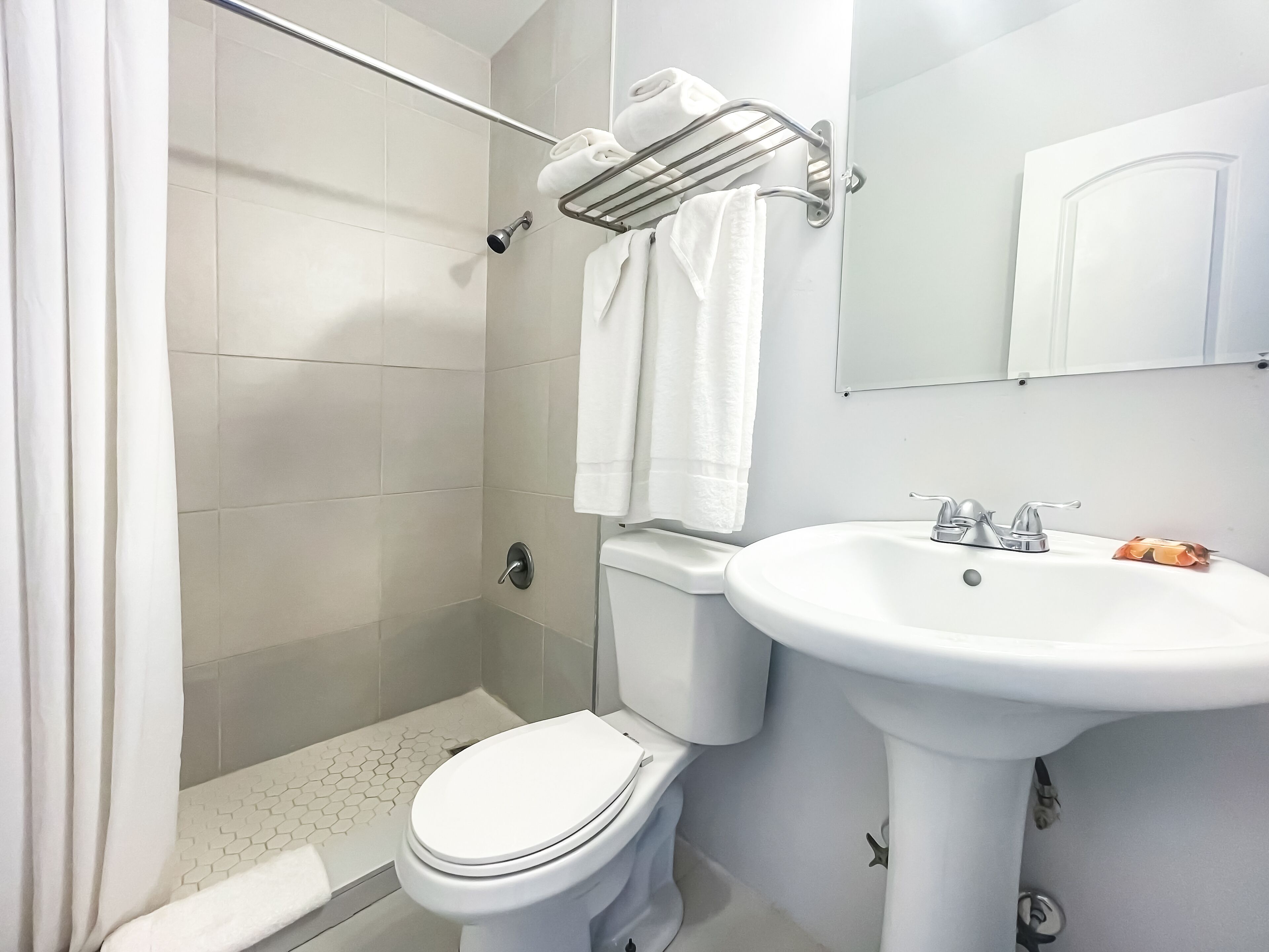 A bathroom with a shower, toilet, sink, and towel rack.