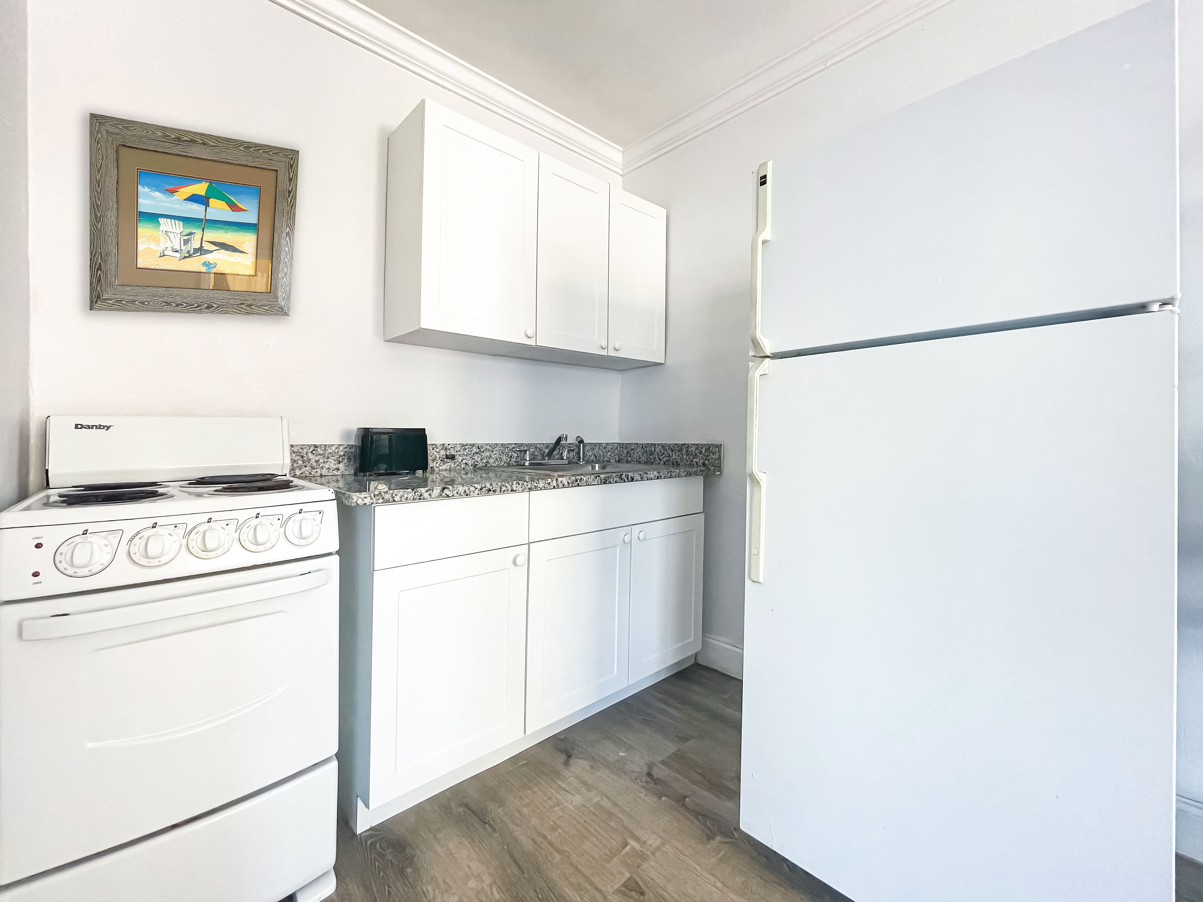 A kitchen with white cabinets, a Danby stove, a black toaster, and a framed beach painting.