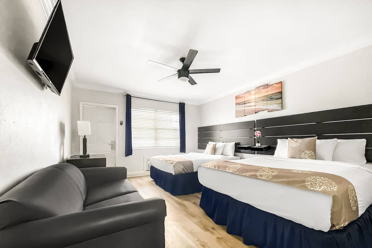 A hotel room with a bed, a desk, a chair, a TV, and a ceiling fan.