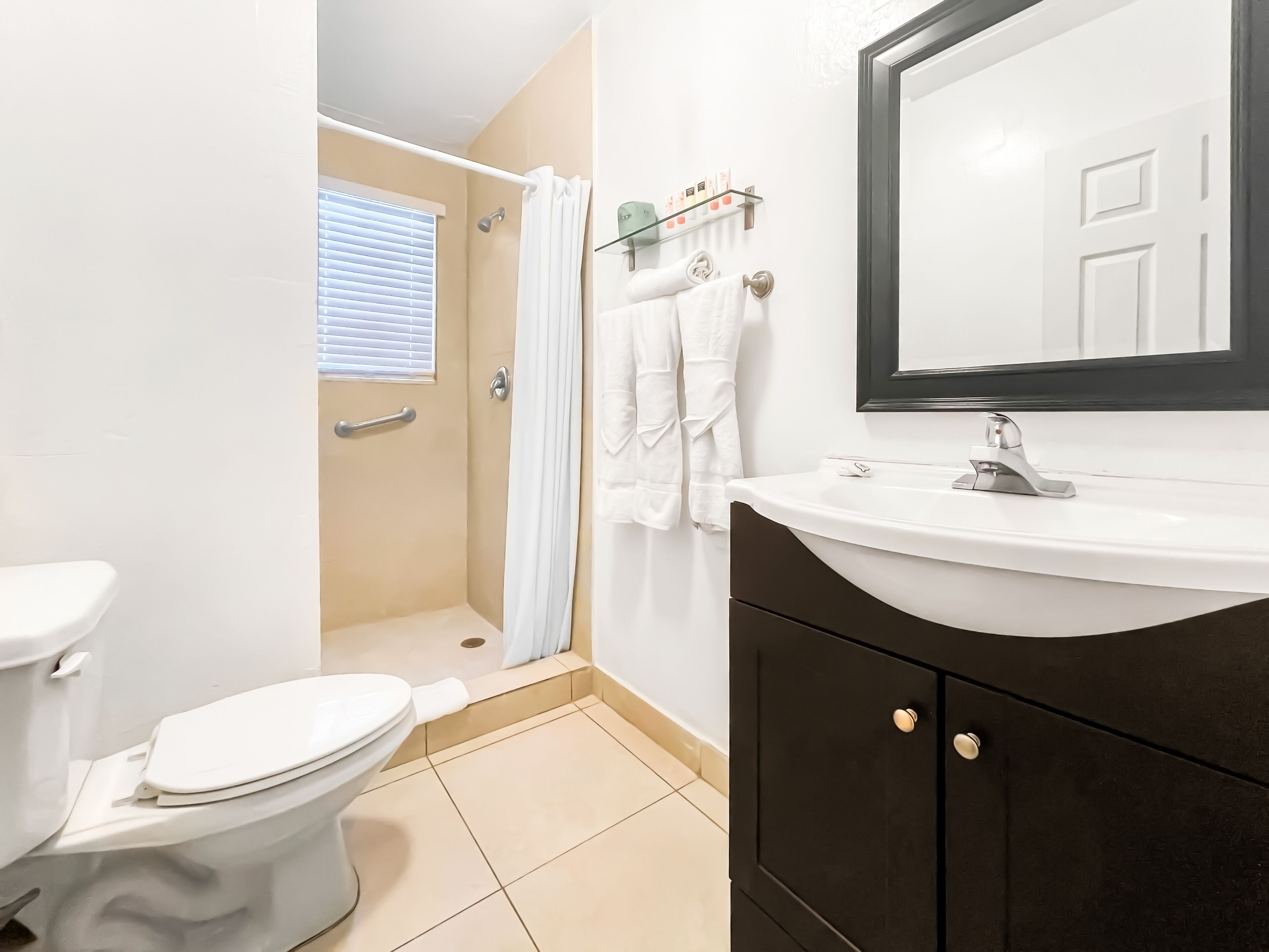 A bathroom with a toilet, shower, sink, and a mirror.