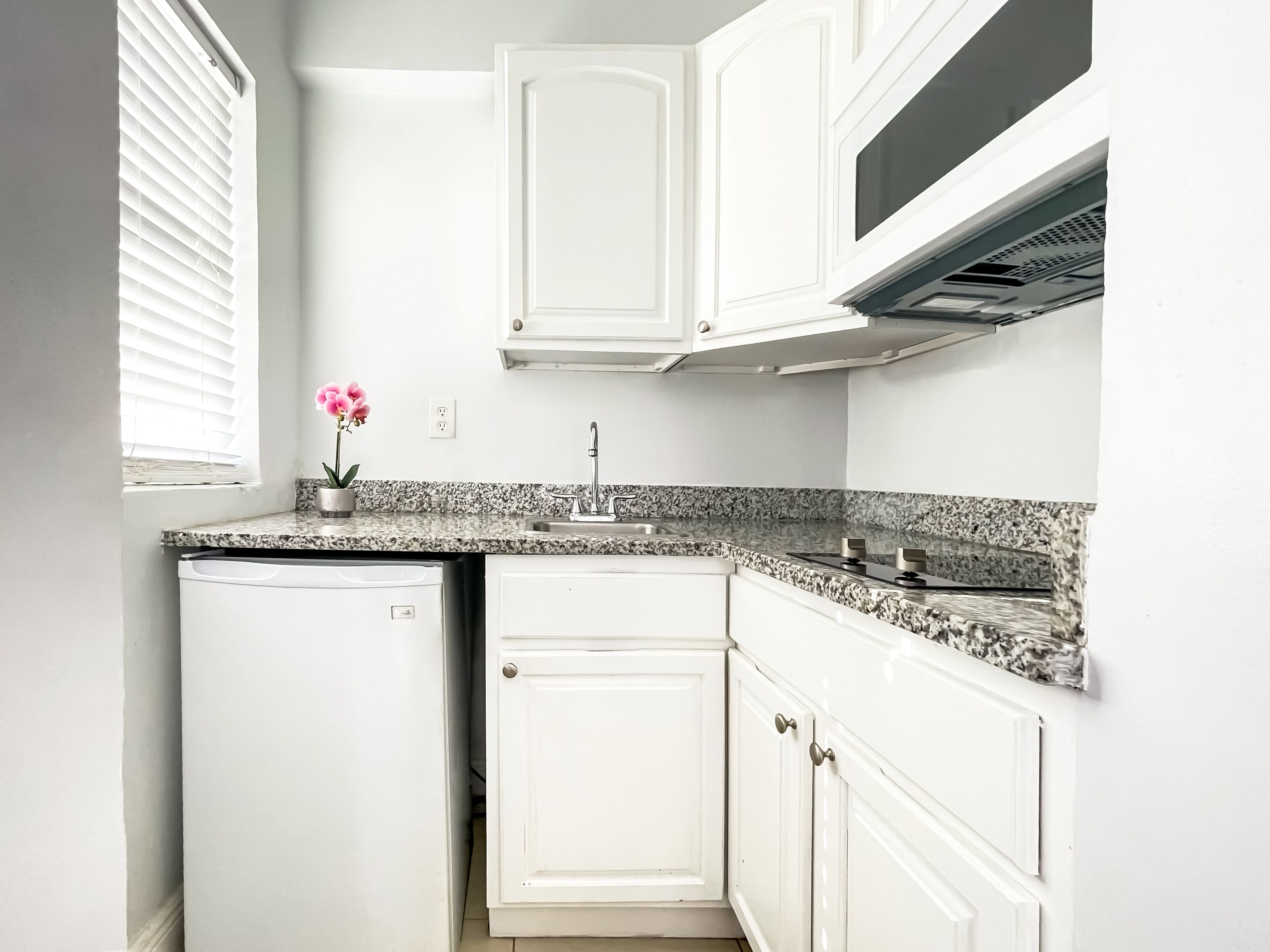 A kitchen with white cabinets, a granite countertop, a built-in oven, and a window with blinds.