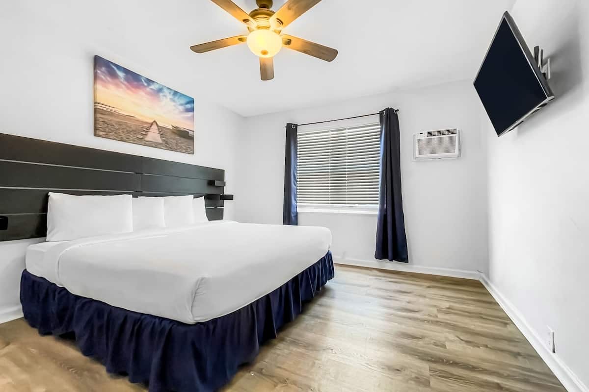 A modern hotel room with a large bed, a ceiling fan, a TV mounted on the wall, and a window with curtains.