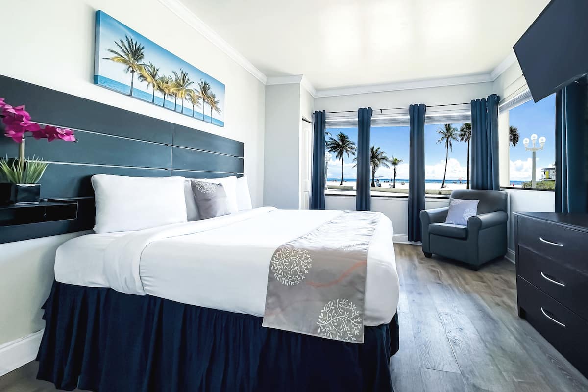 A modern hotel room with a large bed, a seating area, and a view of the beach.