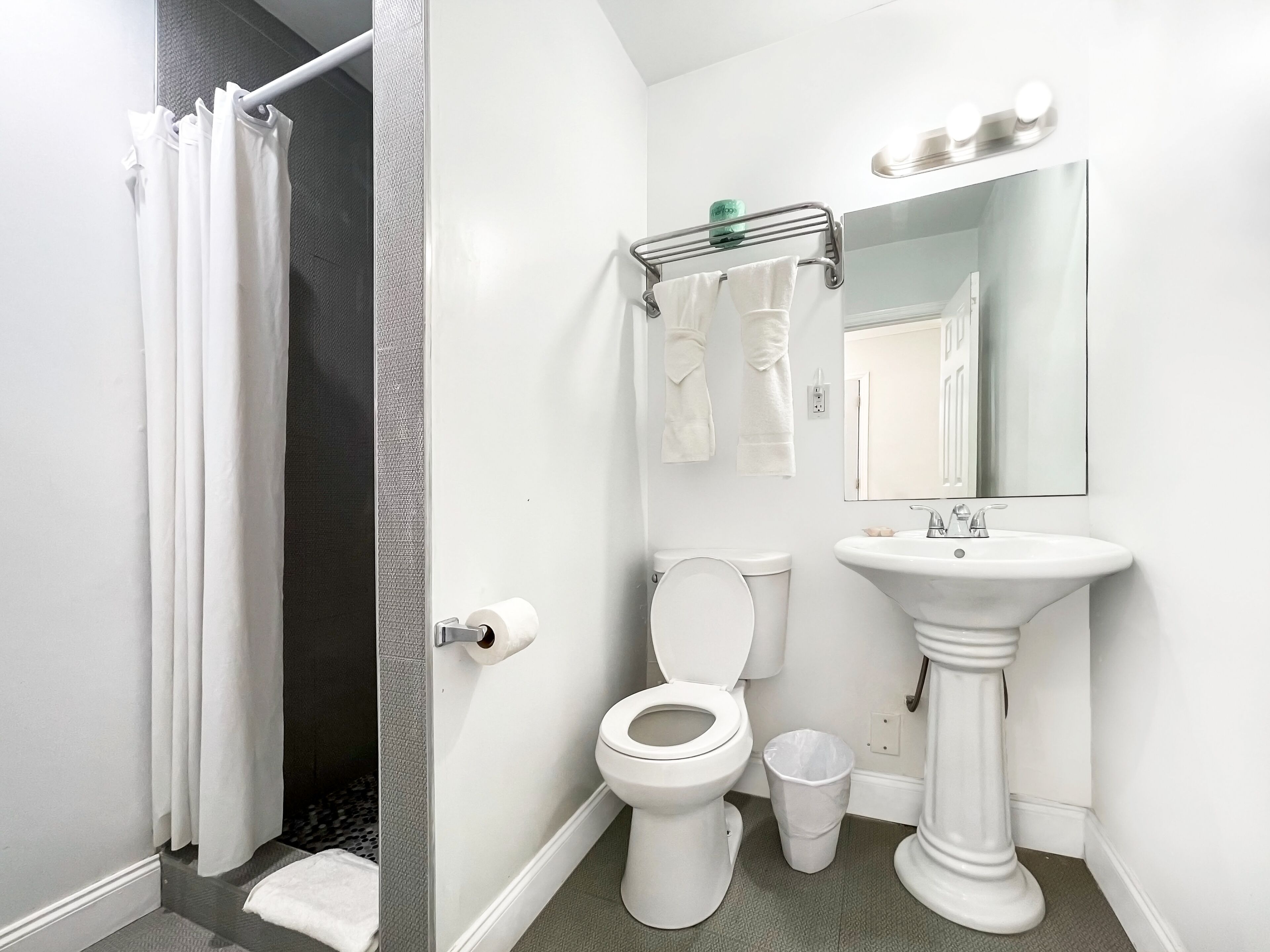 A modern bathroom with a shower, toilet, sink, and a mirror with lights.