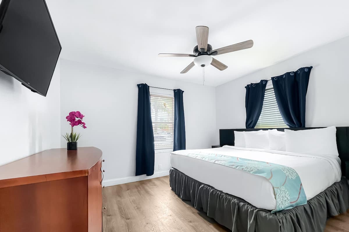 A hotel room with a bed, a desk, a ceiling fan, and a TV on the wall.