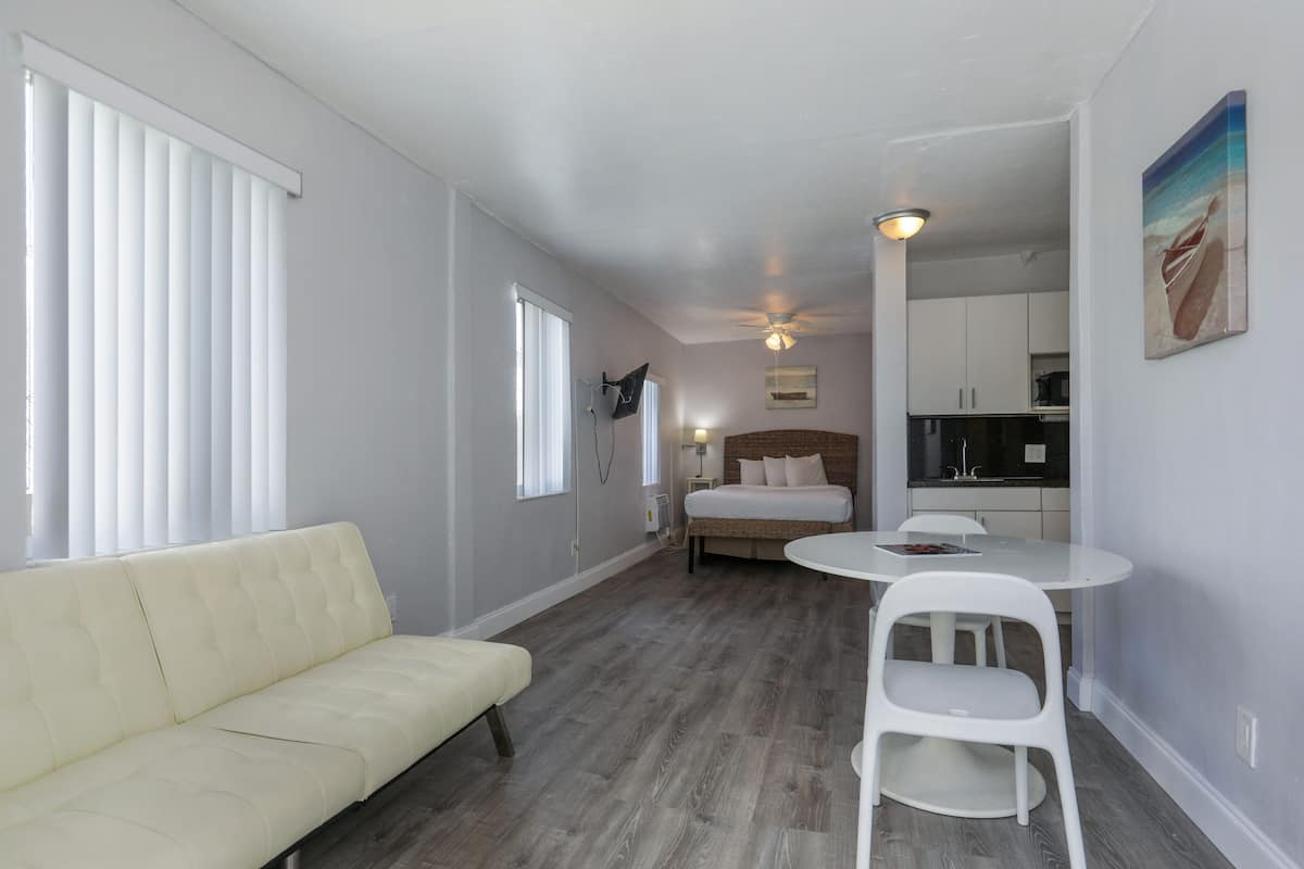 A compact hotel room with a sofa, a small dining table, a bed, and a kitchenette.