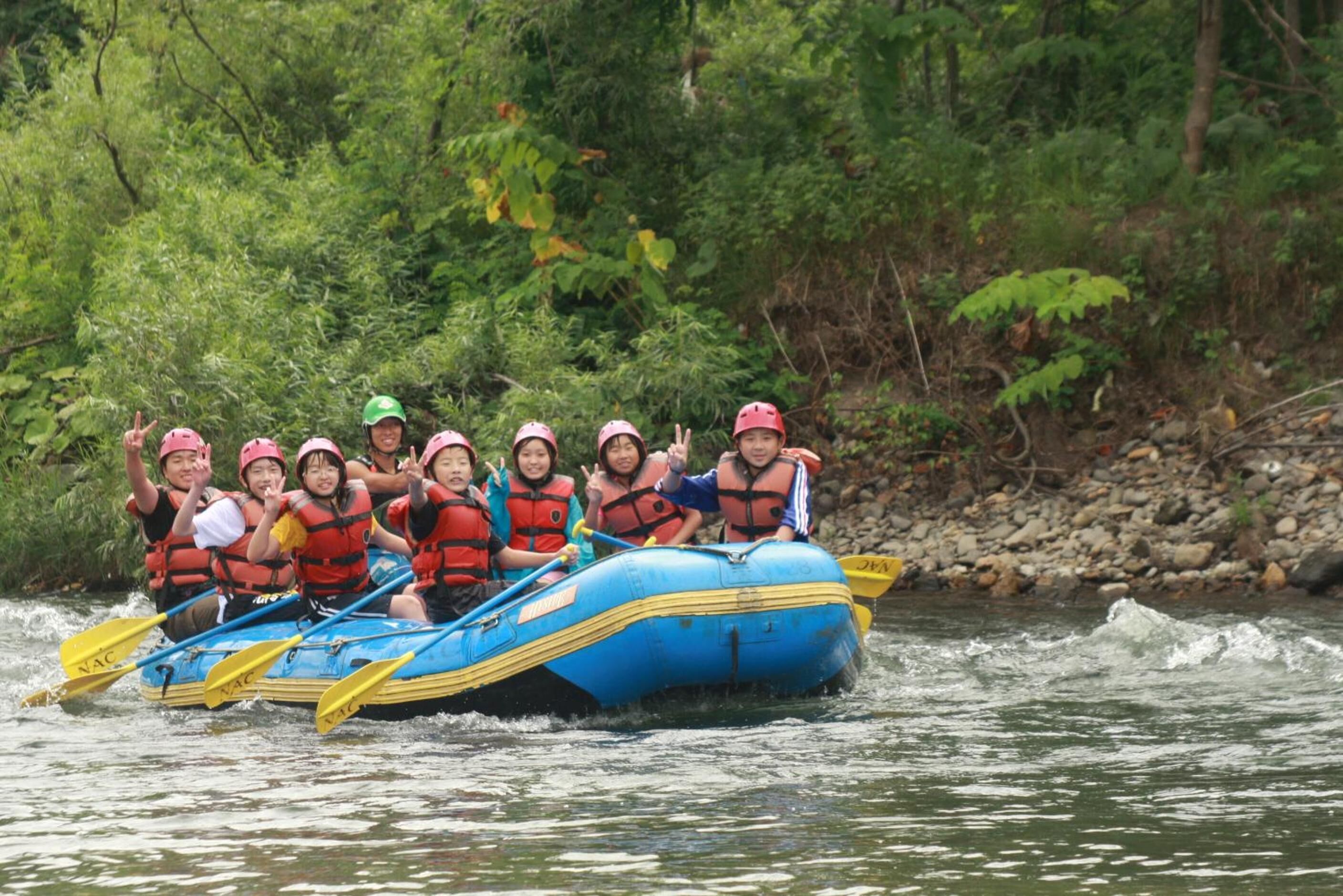 A group of people in a blue raft on a river surrounded by greenery.