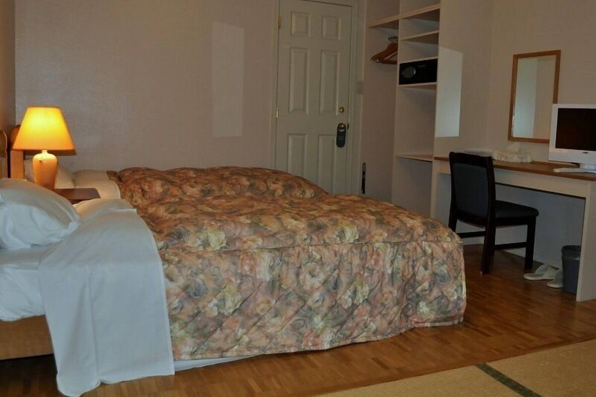 A bedroom with a bed, a desk, a chair, a lamp, and a door.