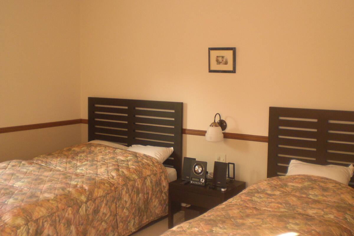 A hotel room with two beds, a nightstand with a lamp, and a framed picture on the wall.