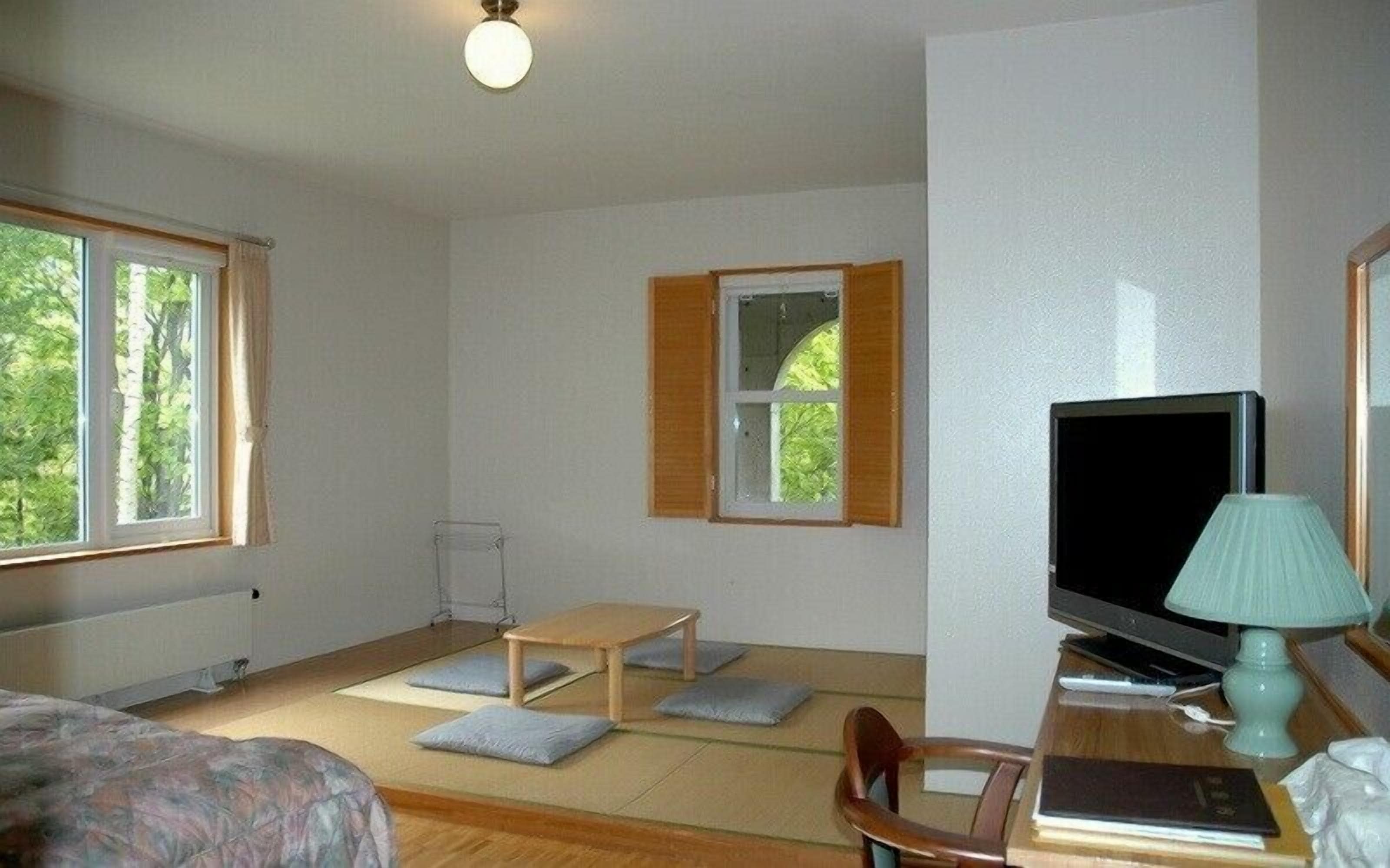 A room with a bed, a small table, a chair, a television, and a lamp.