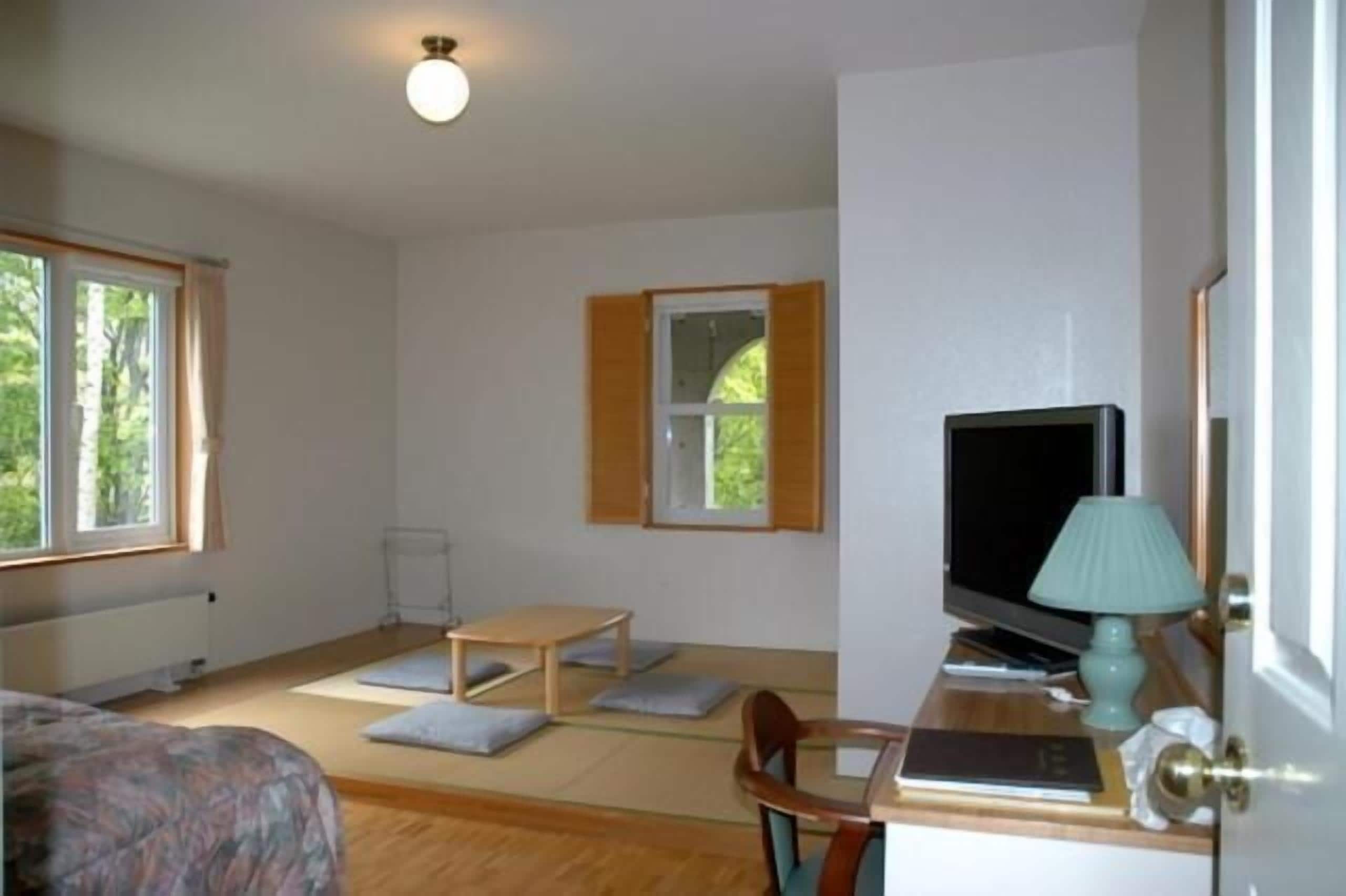 Una habitación con cama, un escritorio con computadora, televisor y ventana con contraventanas de madera.