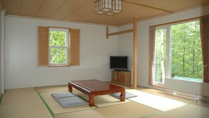 Perinteinen japanilainen huone, jossa on tatamimatto, matala puupöytä, televisio ja suuret ikkunat, joissa on verhot.