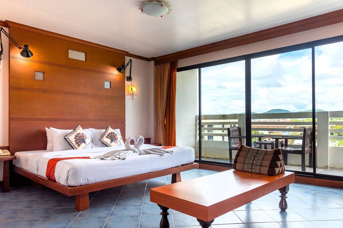 Una habitación de hotel con una cama grande, una mesita de noche de madera, un escritorio y vistas a la ciudad a través de amplios ventanales.