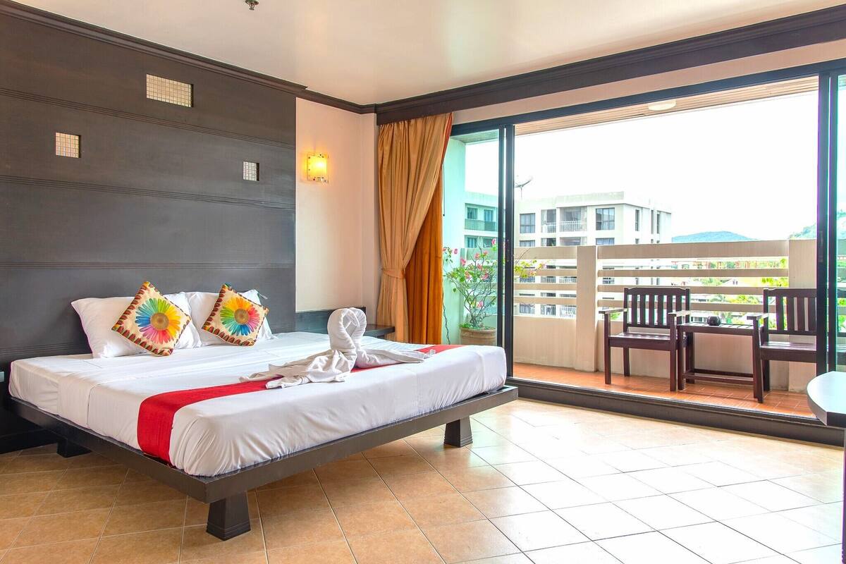 Habitación de hotel con cama, balcón con sillas y vista a edificios.