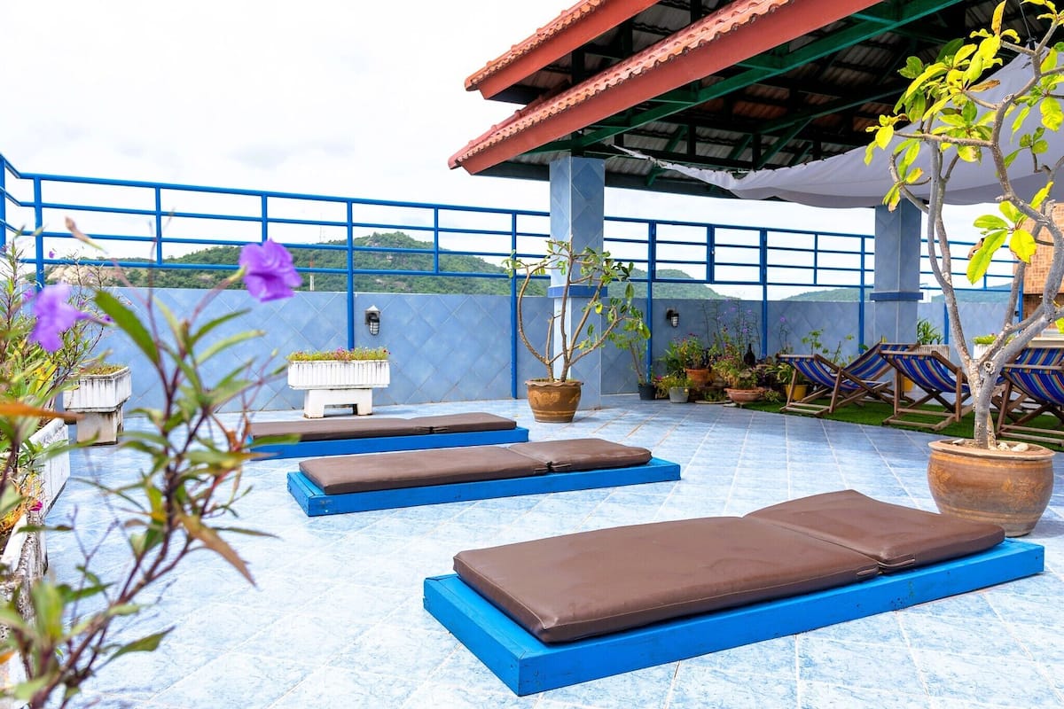 Un área de lounge en la azotea con sillones y cojines azules, plantas en macetas y vistas a las colinas.