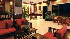 Un vestíbulo amplio con una mesa de recepción, un área de descanso con sofás rojos y diversas plantas.