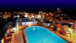 Una piscina en la azotea con sillones reclinables y vistas a la ciudad de noche.